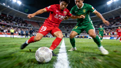 中超联赛直播画面，上海海港队红色球衣球员与北京国安队绿色球衣球员在中场争抢球权